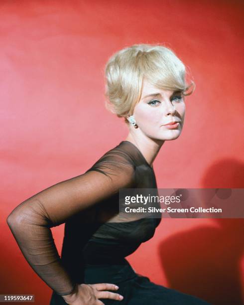 Elke Sommer, German actress, wearing a black dress with black chiffon sleeves in a studio portrait, against a red background, circa 1965.