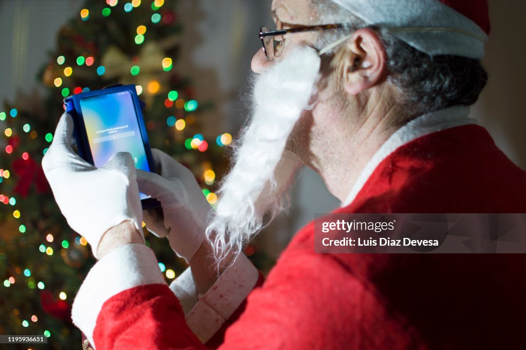 Man dressed as santa claus using smart phone in front of christmas tree