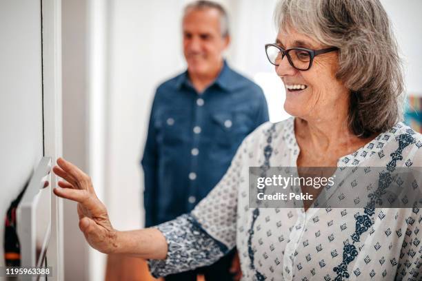 femme aîné utilisant le panneau d'écran tactile de domotique dans la maison de soins infirmiers - température photos et images de collection