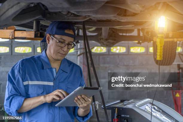 car mechanic examining car suspension of lifted automobile at repair service station - chassis stock pictures, royalty-free photos & images