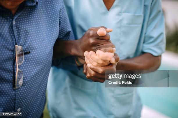 männliche krankenschwester unterstützt senior mann im pflegeheim - nurse with old male patient home care stock-fotos und bilder