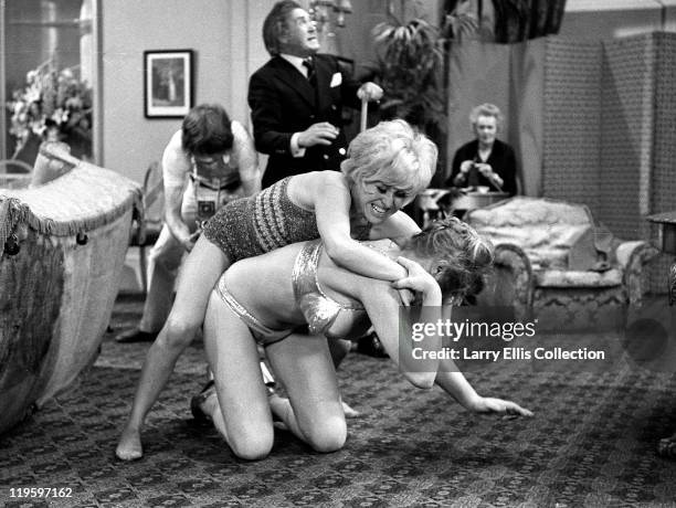 English actors Peter Butterworth and Robin Askwith watch feuding actresses Margaret Nolan and Barbara Windsor in the film 'Carry On Girls', 1973.