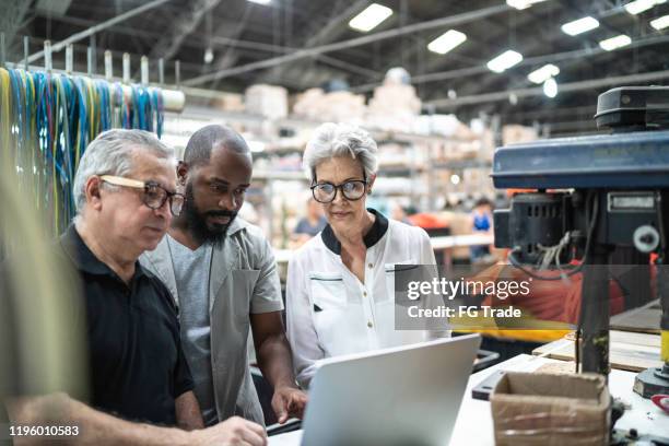 compañeros de trabajo que utilizan computadora portátil y trabajan juntos en fábrica - industry worker fotografías e imágenes de stock