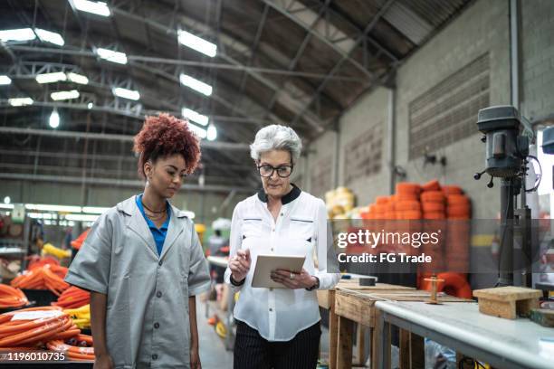 manager using his tablet explaining her employee at industry - baby boomer working stock pictures, royalty-free photos & images