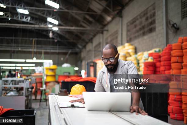 ingénieur travaillant à l'usine utilisant l'ordinateur portatif - african ethnicity stock photos et images de collection