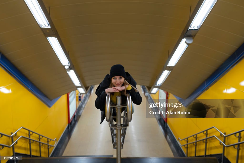 Young blonde girl in the yellow subway with hat and black clothes on the stairs climb on the railing