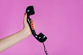 Female hand holding old and retro telephone headset isolated on pink background in studio