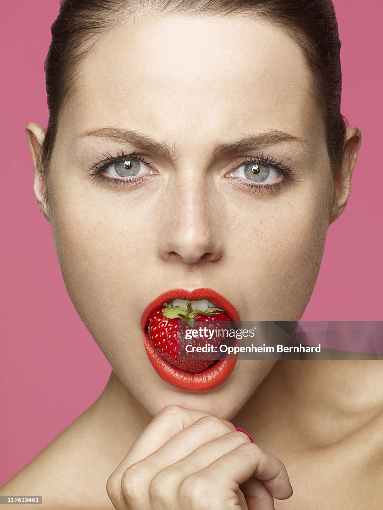 Serious looking female with strawberry in her mout