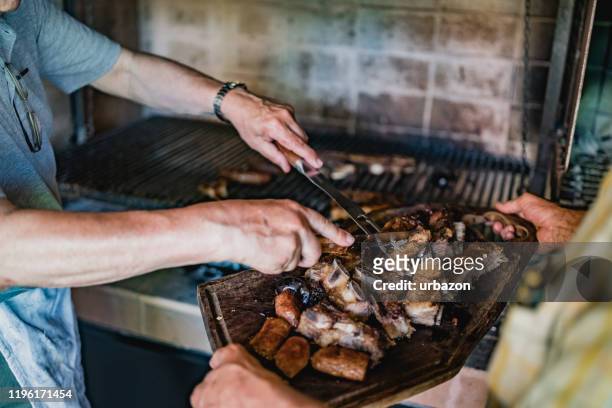 dos hombres sirviendo carne para el almuerzo, asado - argentina steak fotografías e imágenes de stock