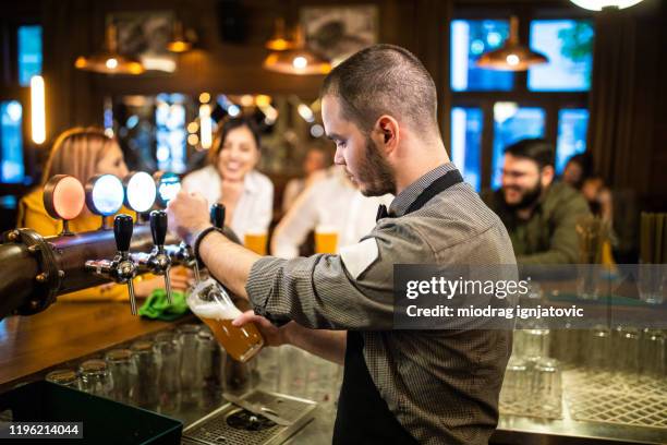 bartender pouring beer from beer tap in a bar - hipster barkeeper stock pictures, royalty-free photos & images