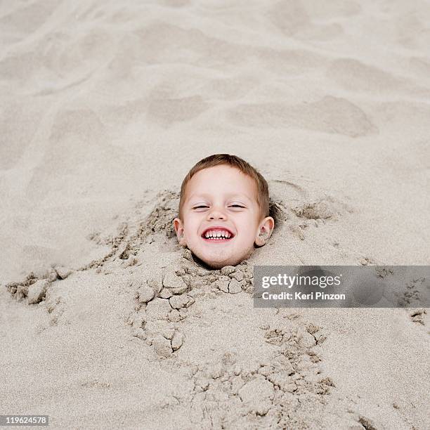 boy (3-5) burried in sand. - head in sand stock-fotos und bilder