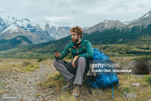 man using smartphone while hiking in torres del paine national park - torres del paine national park imagens e fotografias de stock