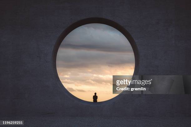 joven solitaria mirando a través de la ventana de hormigón - tranquilidad fotografías e imágenes de stock
