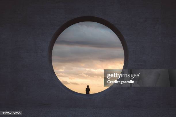 lonely young woman looking through concrete window - windows imagens e fotografias de stock