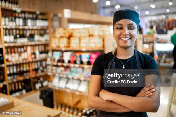 camarera feliz / dueño de negocio de pie con los brazos cruzados en un mercado - franchising fotografías e imágenes de stock