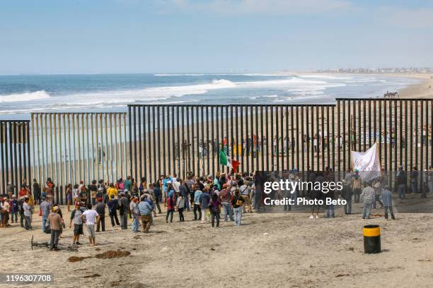 migranti e lavoratori si incontrano lungo entrambi i lati del muro di confine tra stati uniti e messico a tijuana beach, nel nord del messico. - immigrato foto e immagini stock