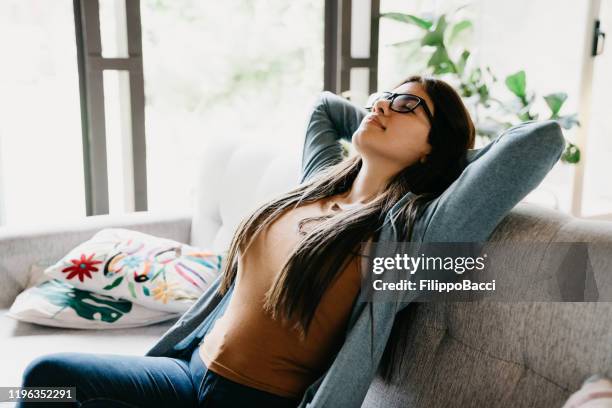 junge erwachsene frau entspannen zu hause, sitzen auf dem sofa - erleichterung stock-fotos und bilder