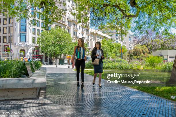 two beautiful young women talking and walking in a public park in the supreme court district at buenos aires city, argentina. - buenos aires city stock pictures, royalty-free photos & images