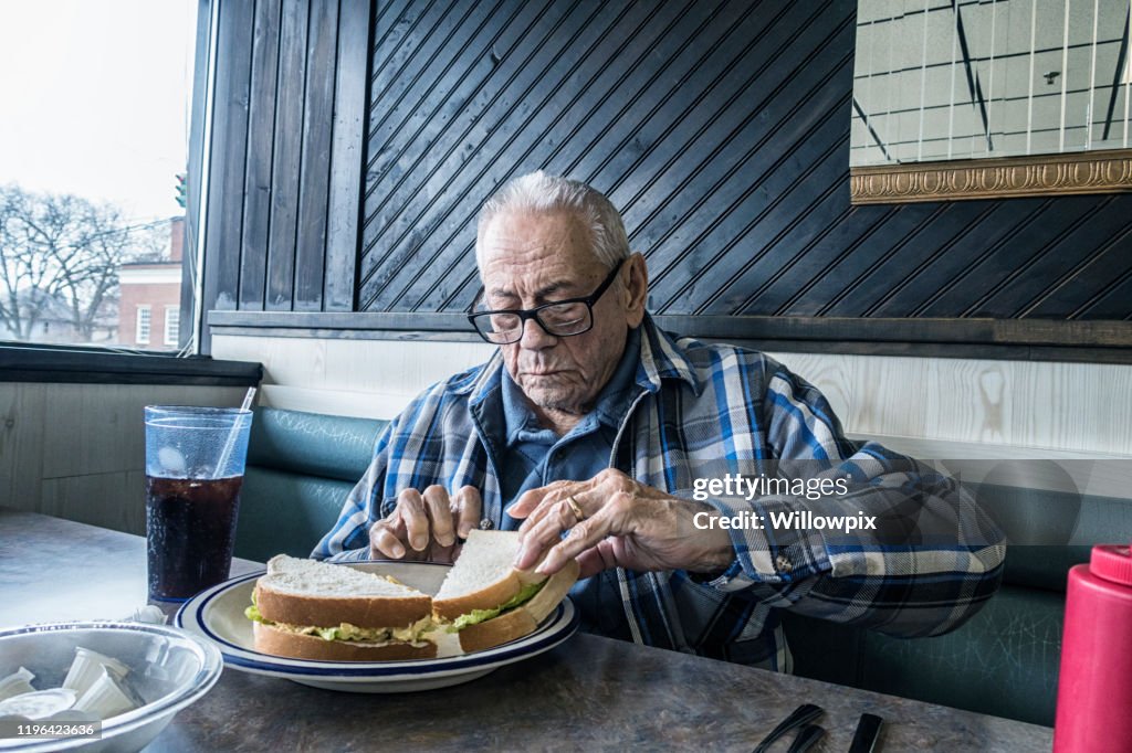 Elderly Man in Restaurant Picking Up Egg Salad Sandwich