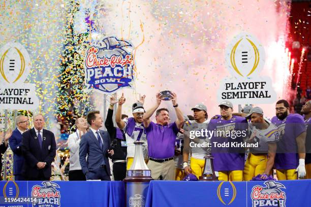 Head coach Ed Orgeron of the LSU Tigers holds the Chick-fil-A Peach Bowl trophy on the podium with the team after winning the Chick-fil-A Peach Bowl...