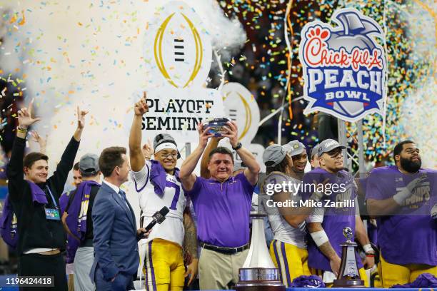 Head coach Ed Orgeron of the LSU Tigers holds the Chick-fil-A Peach Bowl trophy on the podium with the team after winning the Chick-fil-A Peach Bowl...