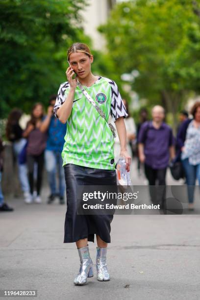 Guest wears a Nike white, black and neon-green top of the Nigerian Football Federation, a shiny metallic-tone crossbody bag, a black leather skirt,...