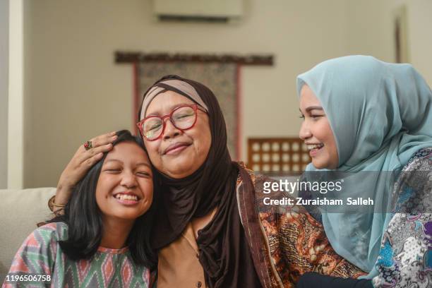 a portrait of happy asian muslim young girl with mother and grandmother sitting at home during hari raya celebration - islam stock pictures, royalty-free photos & images