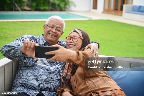 an happy smiling indonesian senior couple sitting on wooden bench at home - malay lover stock pictures, royalty-free photos & images