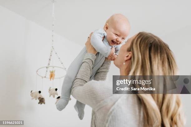 mother throwing baby boy in air in bedroom - mom stockfoto's en -beelden
