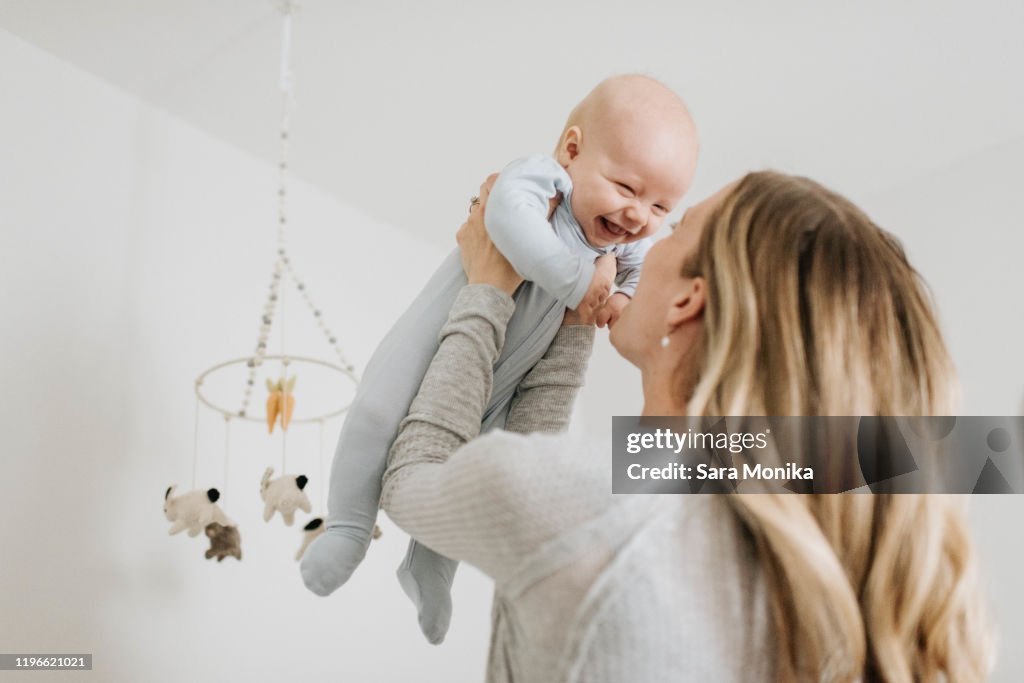 Mother throwing baby boy in air in bedroom