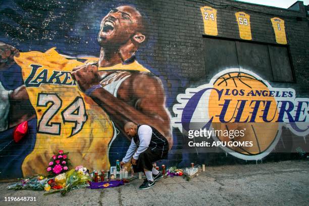 Luis Villanueva lights a candle in front of a Kobe Bryant mural in downtown Los Angeles on January 26, 2020. - Nine people were killed in the...