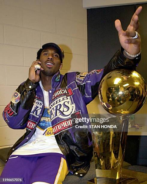 Kobe Bryant of the Los Angeles Lakers talks on his cell phone next to the NBA championship trophy after winning game five of the NBA Finals against...