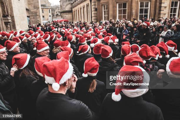 groep feestelijke koorzangers verzamelen buiten bad kathedraal alle dragen van santa hoeden voordat zingen carols aan de wachtende menigte van shoppers in bath, somerset, verenigd koninkrijk - flashmob stockfoto's en -beelden