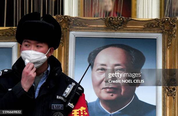 Security guard wearing a facemask to help stop the spread of a deadly virus which began in Wuhan, stands beside a portrait of the late Chinese...