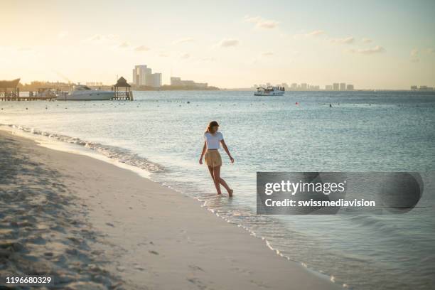 joven caminando en la playa al atardecer - cancun fotografías e imágenes de stock