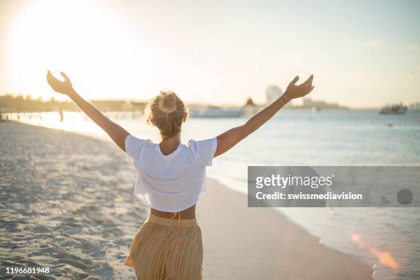 cheerful young woman embracing nature at sunset; female standing on beach arms outstretched - cancun beautiful stock pictures, royalty-free photos & images