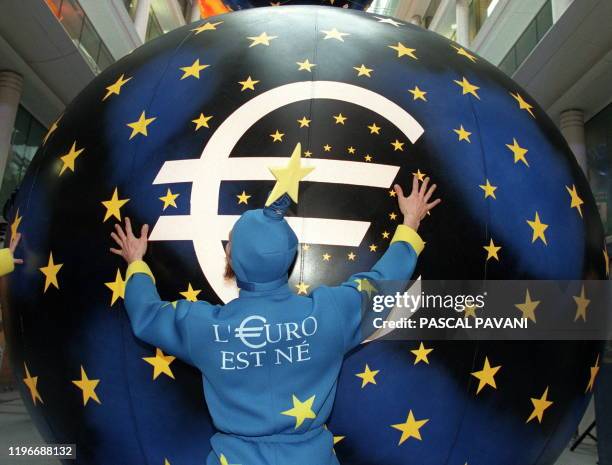 Un artiste habillé aux couleurs de l'euro pousse une boule géante, le 04 janvier au siège de la banque Paribas à Paris, à l'issue de la parade des...