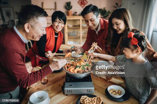 drei generationen von fröhlichen asiatischen familie feiern chinesisches neujahr und genießen traditionelle chinesische poon choi auf wiedersehen abendessen - chinese family taking photo at home stock-fotos und bilder