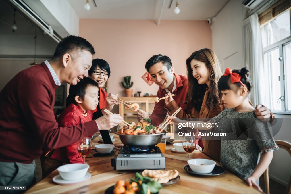 Three generations of joyful Asian family celebrating Chinese New Year and enjoying traditional Chinese poon choi on reunion dinner