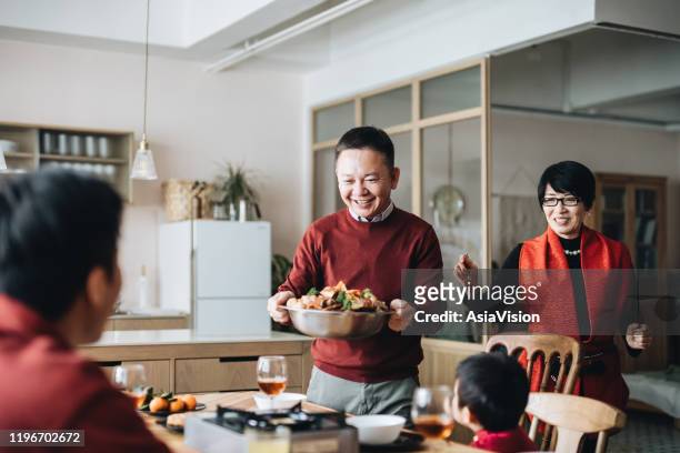 Three generations of joyful Asian family celebrating Chinese New Year and grandparents serving traditional Chinese poon choi on reunion dinner