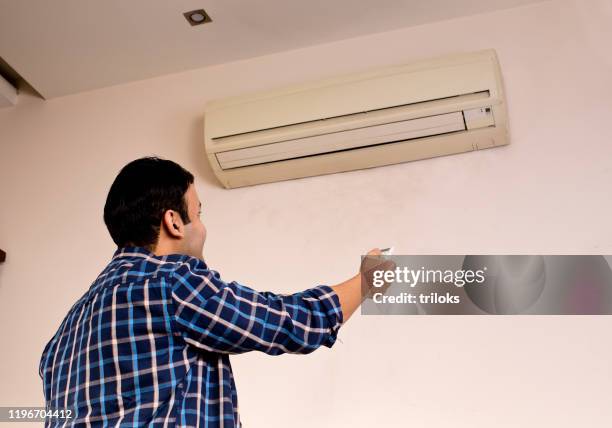 man adjusting the temperature of air conditioner using remote control - hvac stock pictures, royalty-free photos & images