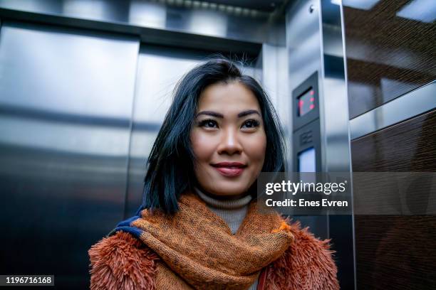 asian woman checking herself out in elevator mirror - elevator stock pictures, royalty-free photos & images