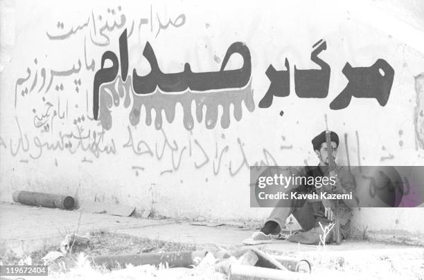 An Iraqi Shia clergyman, opposer of Saddam Hussein and fighting alongside the Iranian forces, armed with a G-3 automatic assault rifle, sits in front...