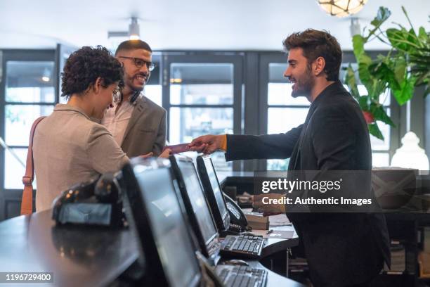 young business couple checking in at hotel and receptionist man helping them. - reception desk stock pictures, royalty-free photos & images