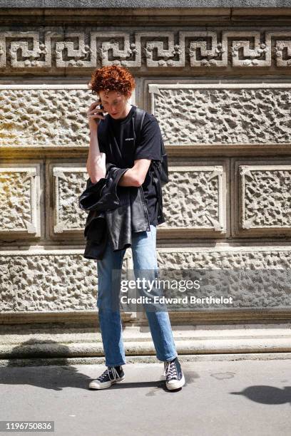 Guest wears a black Patagonia t-shirt, a black leather backpack, blue jeans, black sneakers, outside Bode, during Paris Fashion Week - Menswear...