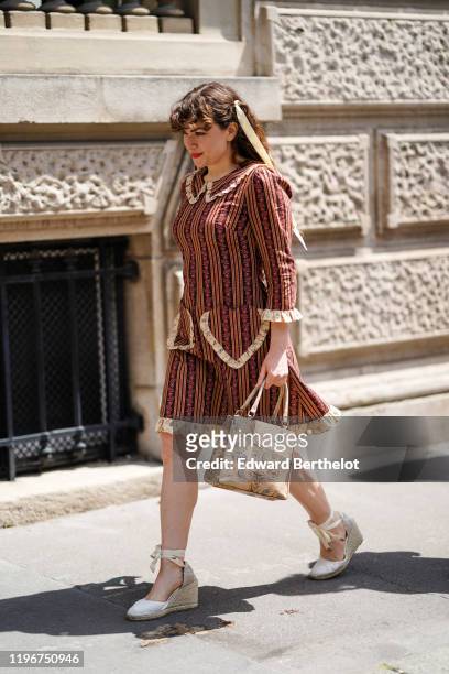 Guest wears a ribbon in the hair, a brown and burgundy dress with stripes and floral print, a beige handbag with sea-shells pattern, white wedge...