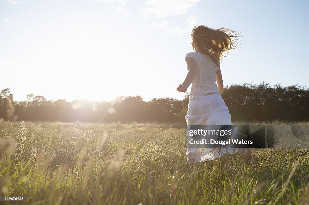 Woman runnning towards sunset through meadow.