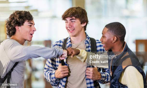 three teenage boys standing in library, fist bumping - teenagers greeting stock pictures, royalty-free photos & images