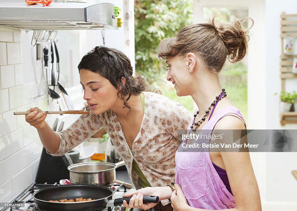 Woman tasting pasta sauce while friend looks on.