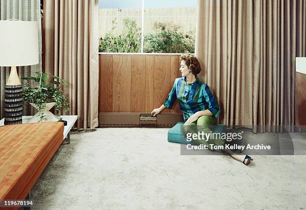 young woman sitting on cushion adjusting radiator's knob - 1950 1959 stock pictures, royalty-free photos & images